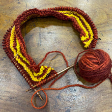 the start of a top down jumper lies on a wooden surface. The knitting is in rust and yellow stripes.